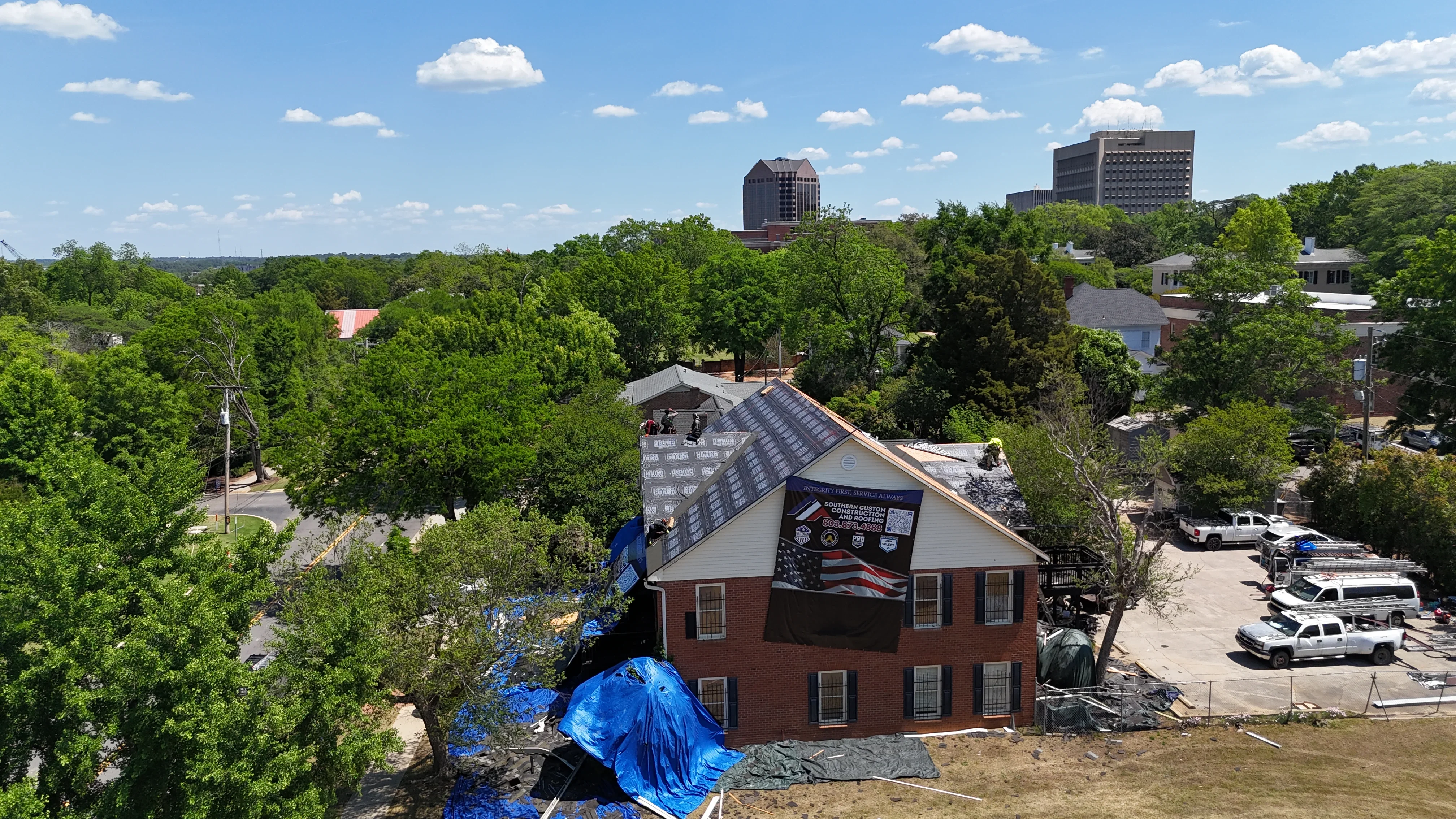 Pitched asphalt shingle roof installation on two-story brick building with protective tarping