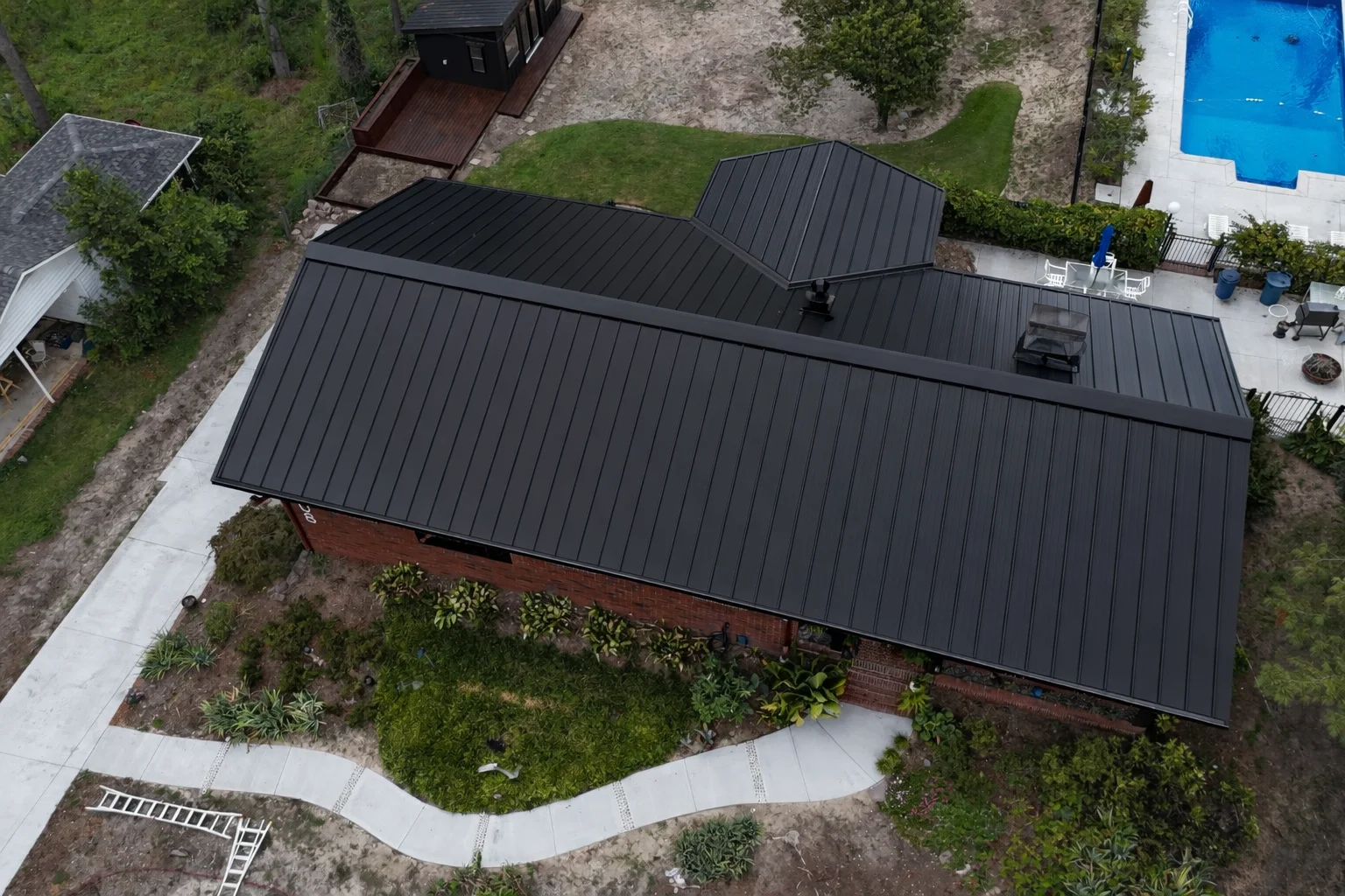 Aerial view of standing seam metal roof on brick home with multiple planes and vertical panel lines