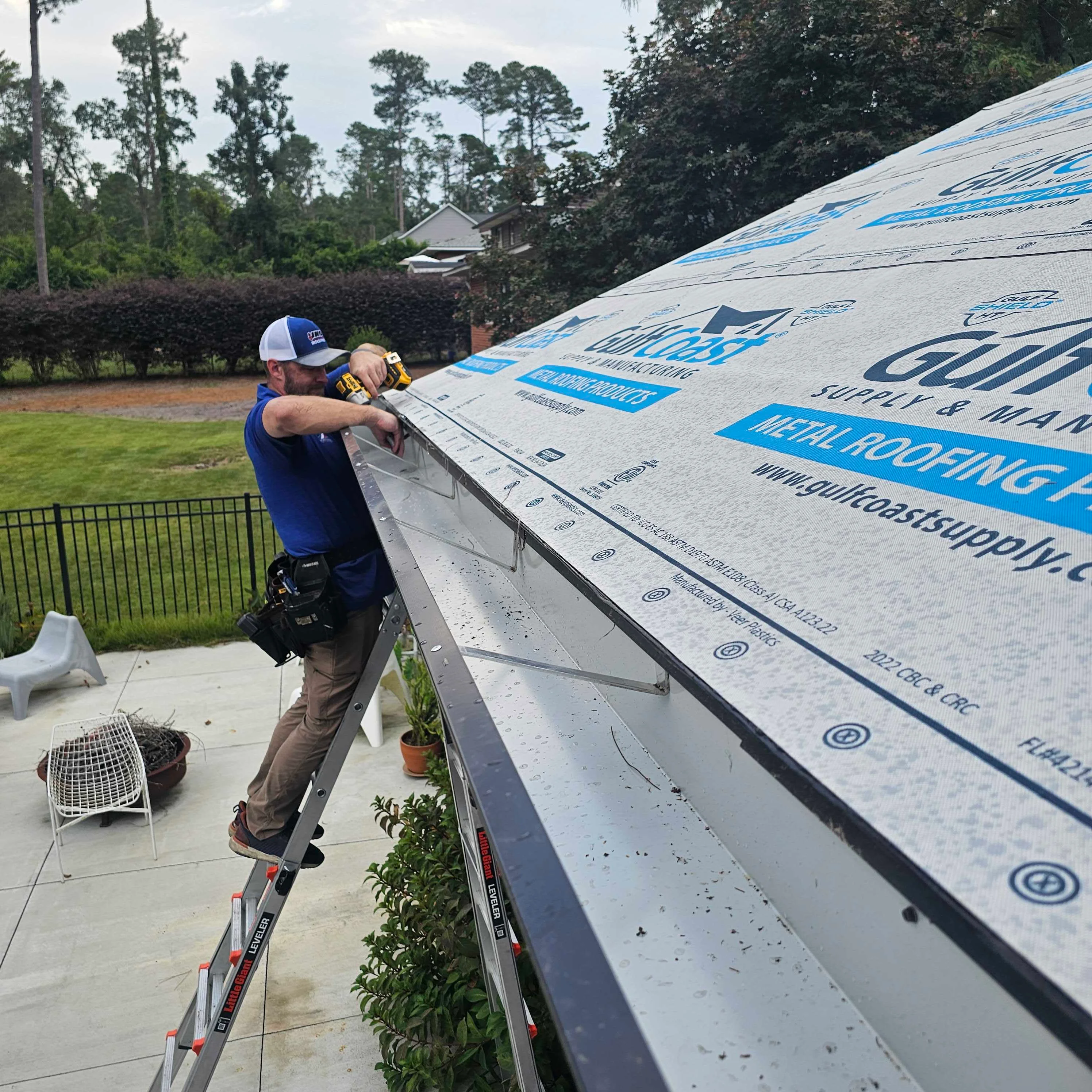 Roofer installing blue synthetic underlayment on residential roof with proper fastening