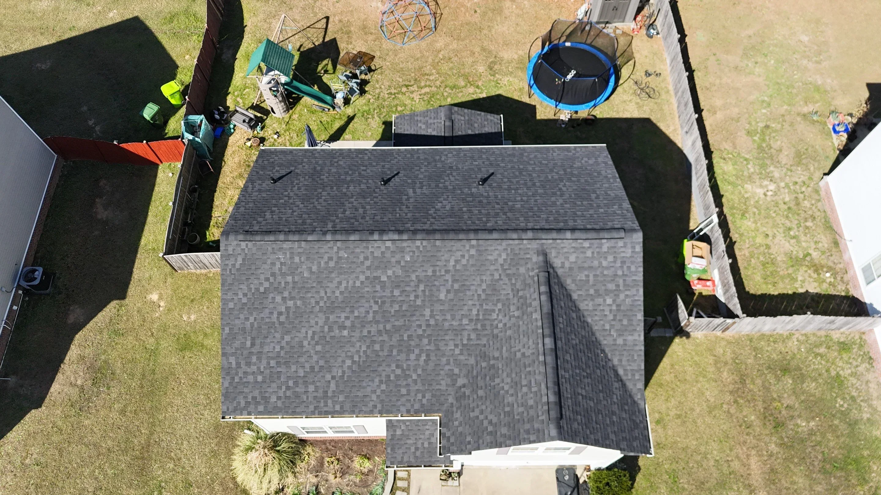 Aerial view of residential roof with charcoal gray asphalt shingles, ridge vent, and roof penetrations