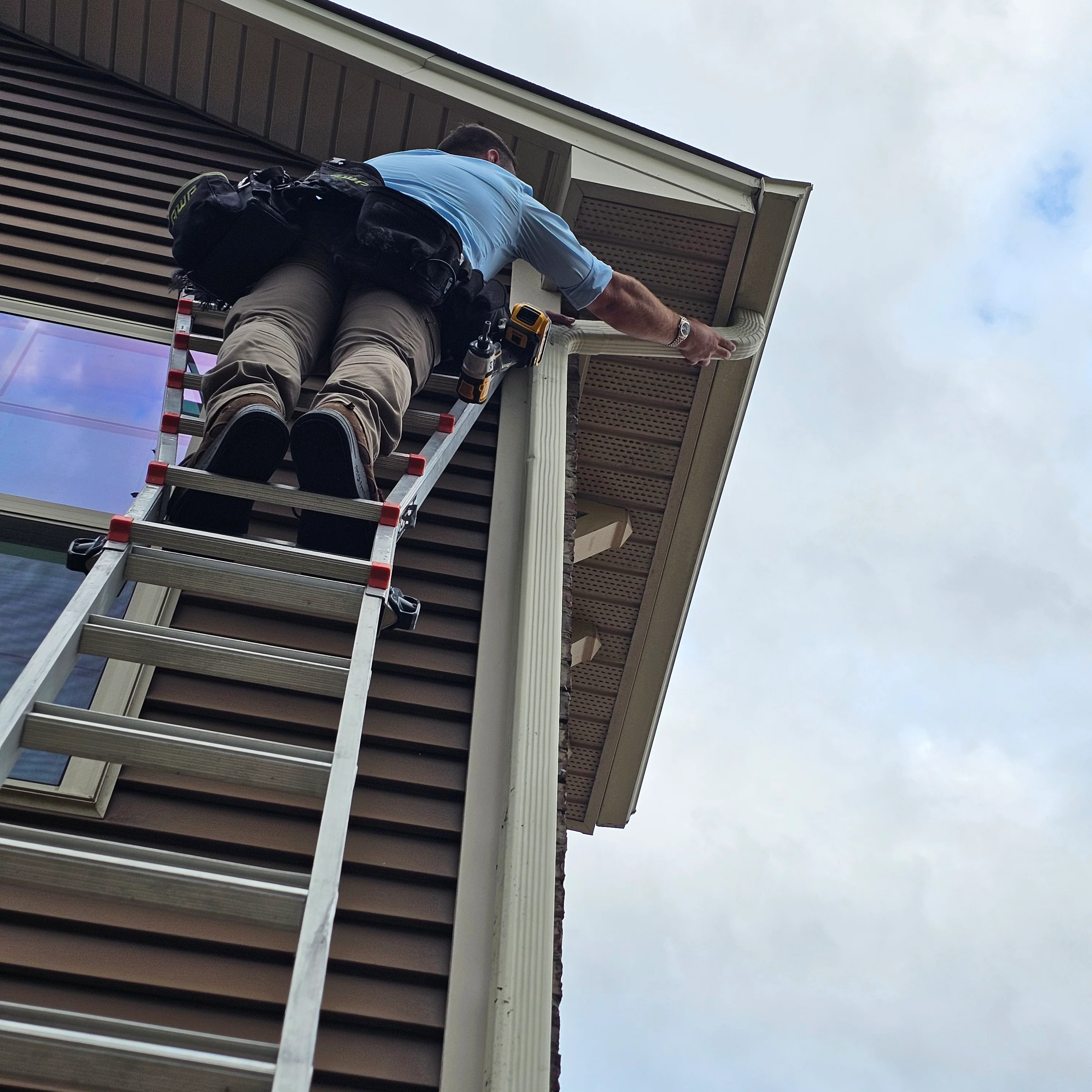 Technician installing vinyl soffit and fascia trim on residential eave using ladder