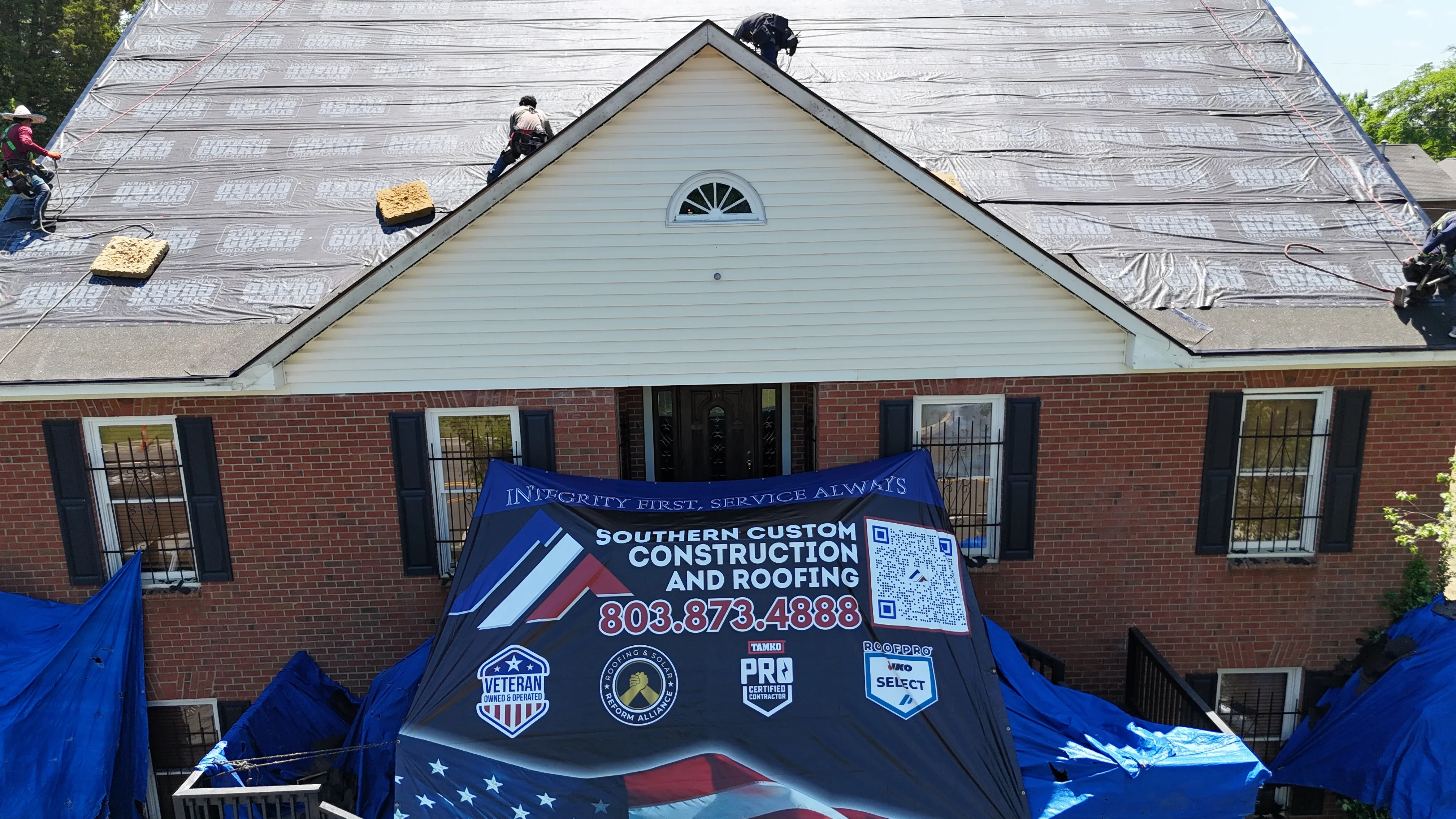 Roofers installing asphalt shingles on residential home with protective underlayment and safety equipment