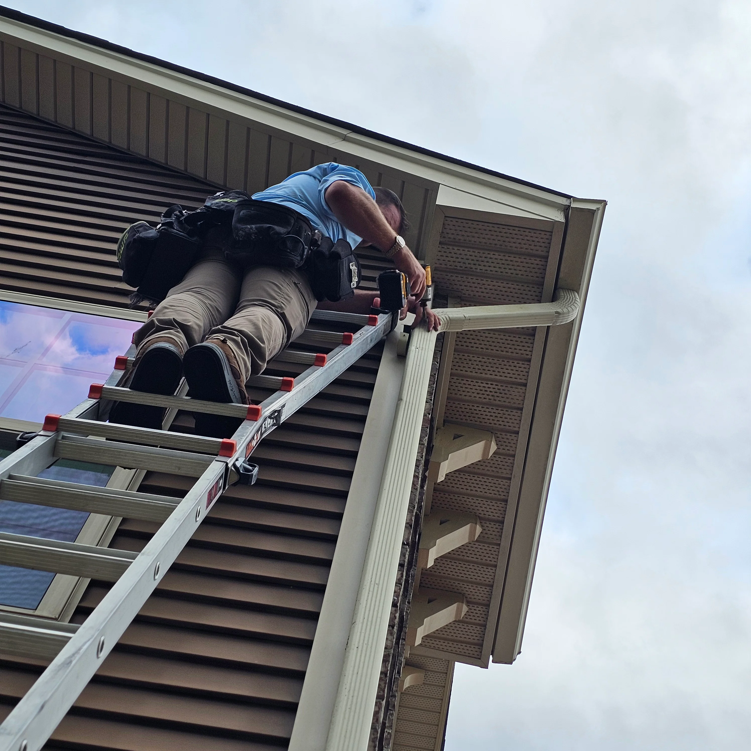 Worker installing white vinyl soffit and fascia trim on residential roofline with metal roof panels