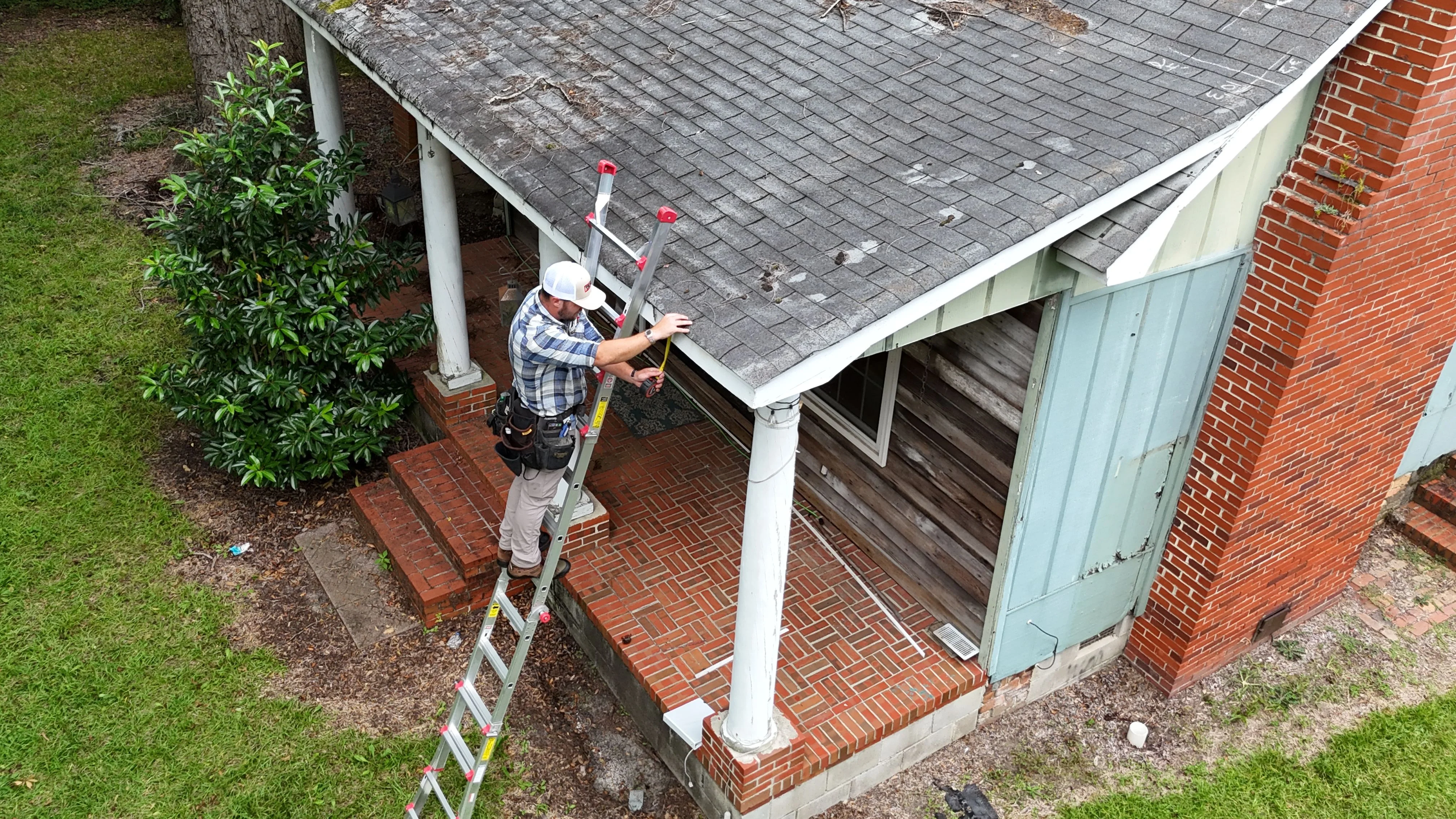 A Southern Custom Construction and Roofing contractor inspecting the shingles and flashing on a brick ranch home in Cayce, SC. The inspector examines the roof surface and gutters for storm damage and wear.