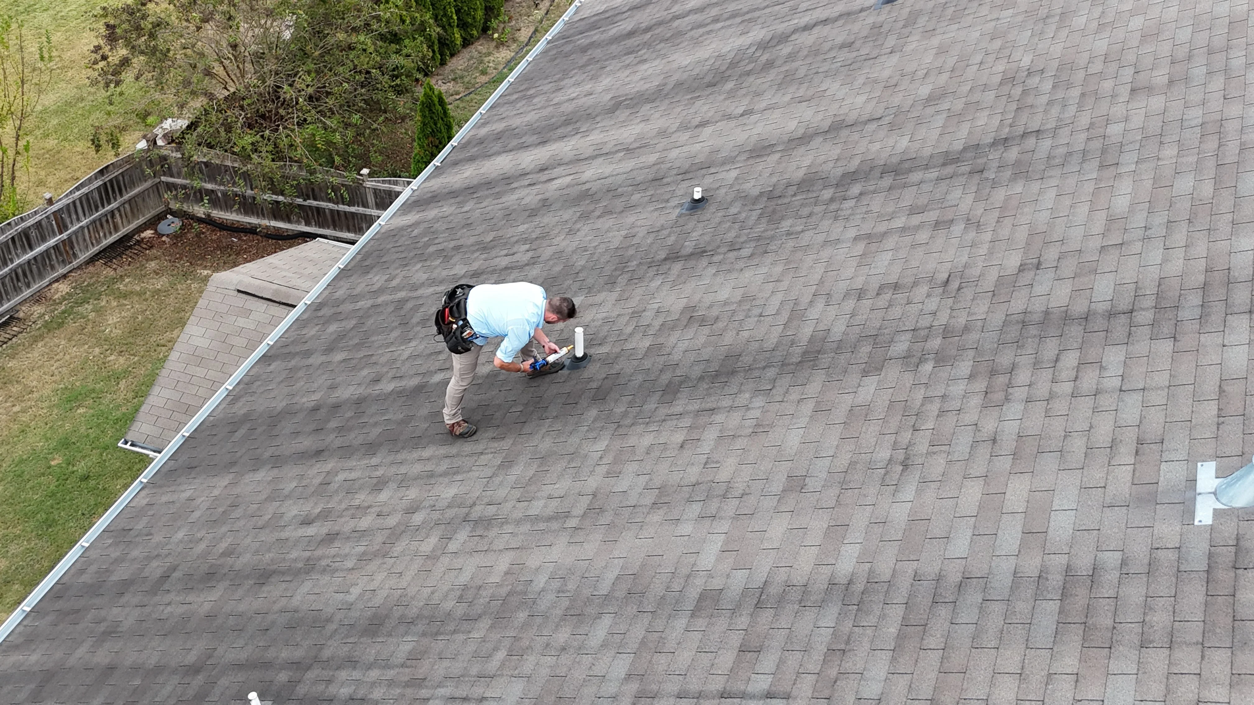 A Southern Custom Construction and Roofing technician inspecting shingles and flashing on a residential roof in Cayce, SC. The image shows a close-up of the roof surface with visible granule wear and a gutter line running along the roofline.
